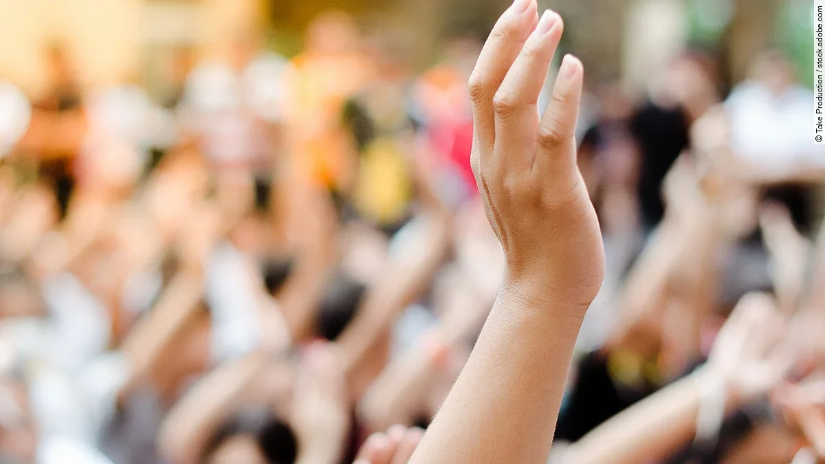 Hochgehobene Hand vor einer Gruppe von Menschen