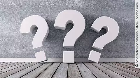 Drei Fragezeichen vor einer grauen Wand 