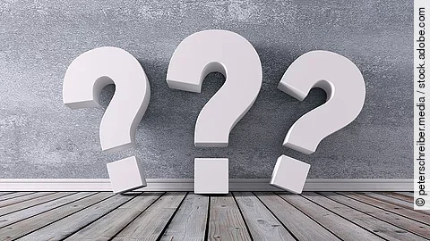 Drei Fragezeichen vor einer grauen Wand 