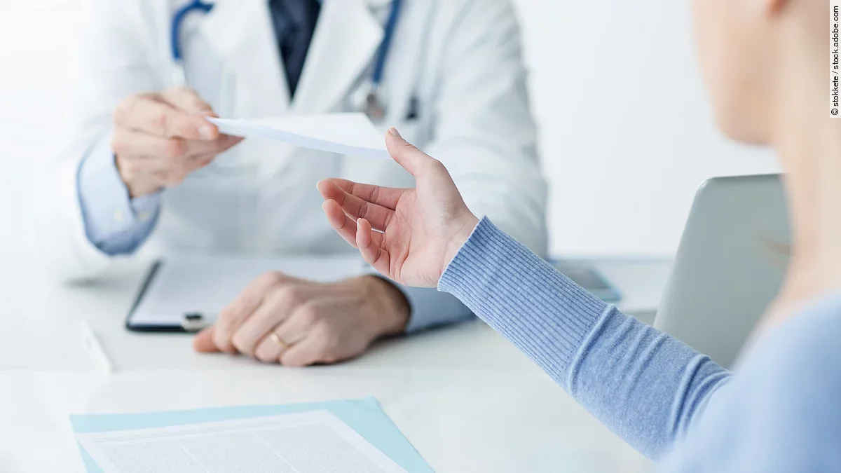 Ein Arzt überreicht einer Patientin ein Dokument.