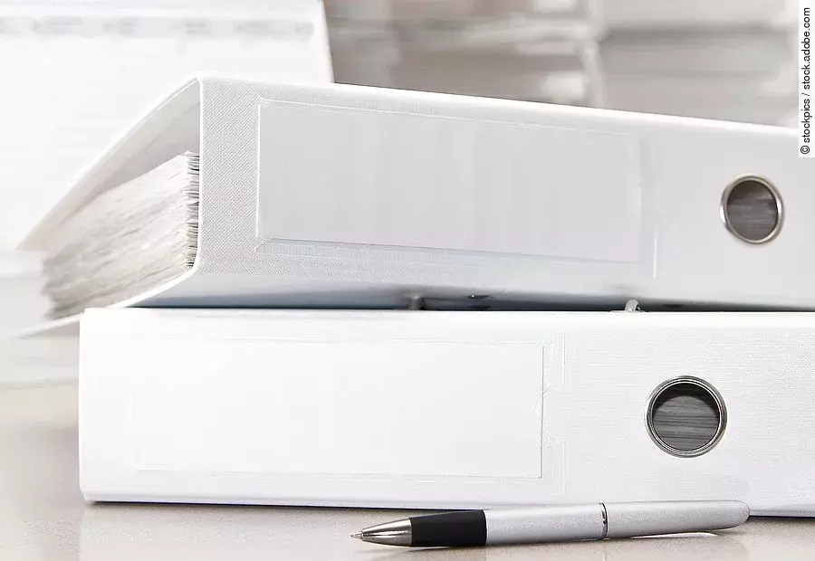 Zwei weiße Aktenordner liegen übereinander. Davor liegt ein silberner Kugelschreiber.