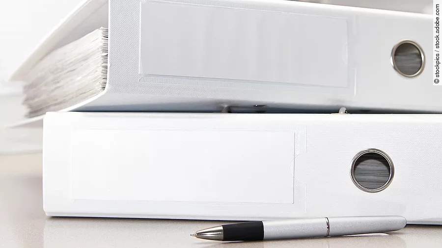 Zwei weiße Aktenordner liegen übereinander. Davor liegt ein silberner Kugelschreiber.