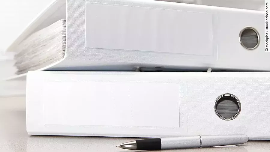Zwei weiße Aktenordner liegen übereinander. Davor liegt ein silberner Kugelschreiber.