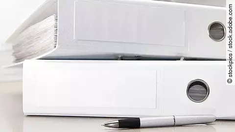 Zwei weiße Aktenordner liegen übereinander. Davor liegt ein silberner Kugelschreiber.