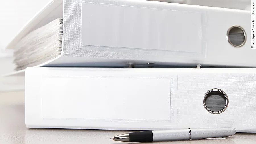 Zwei weiße Aktenordner liegen übereinander. Davor liegt ein silberner Kugelschreiber.