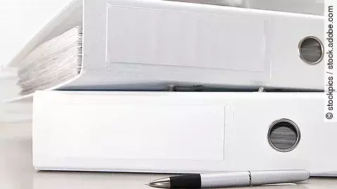 Zwei weiße Aktenordner liegen übereinander. Davor liegt ein silberner Kugelschreiber.