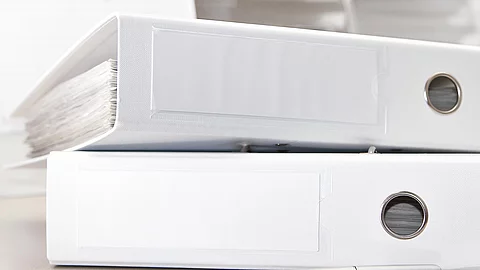 Zwei weiße Aktenordner liegen übereinander. Davor liegt ein silberner Kugelschreiber.