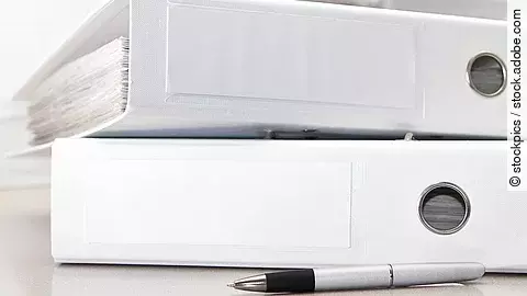 Zwei weiße Aktenordner liegen übereinander. Davor liegt ein silberner Kugelschreiber.