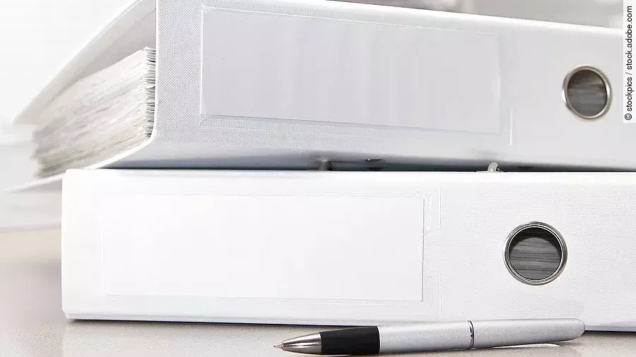 Zwei weiße Aktenordner liegen übereinander. Davor liegt ein silberner Kugelschreiber.