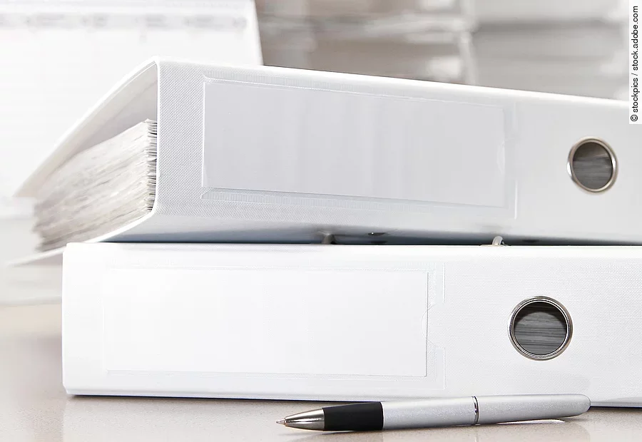 Zwei weiße Aktenordner liegen übereinander. Davor liegt ein silberner Kugelschreiber.