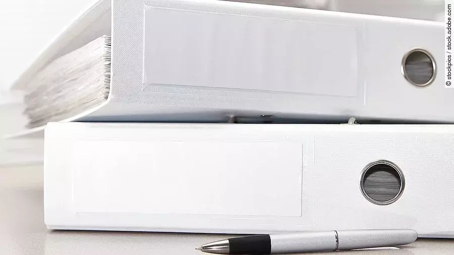 Zwei weiße Aktenordner liegen übereinander. Davor liegt ein silberner Kugelschreiber.