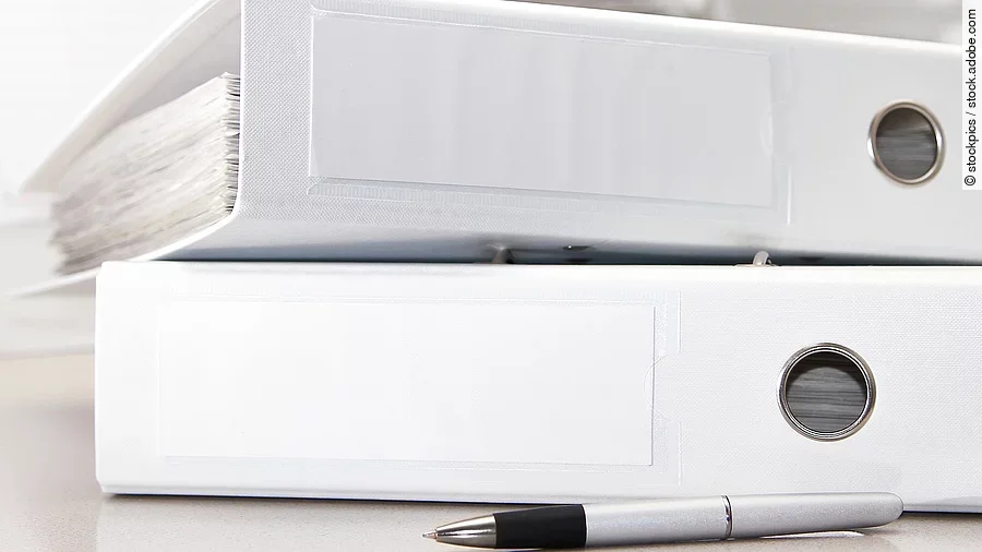 Zwei weiße Aktenordner liegen übereinander. Davor liegt ein silberner Kugelschreiber.