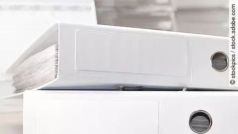 Zwei weiße Aktenordner liegen übereinander. Davor liegt ein silberner Kugelschreiber.