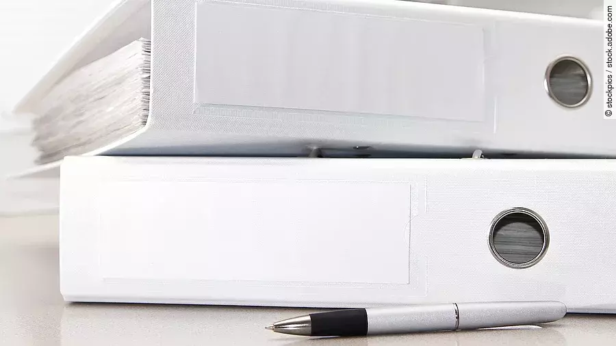 Zwei weiße Aktenordner liegen übereinander. Davor liegt ein silberner Kugelschreiber.