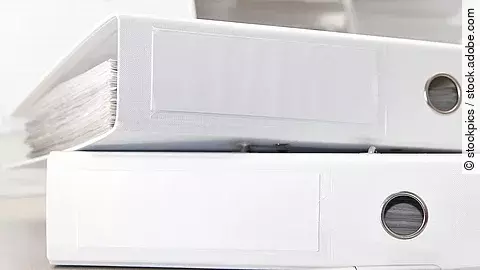 Zwei weiße Aktenordner liegen übereinander. Davor liegt ein silberner Kugelschreiber.