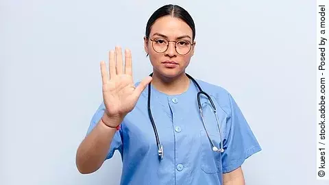 Stop Eine Frau im Kasack und mit Stethoskop schaut ernst und hebt die Hand als Stopzeichen