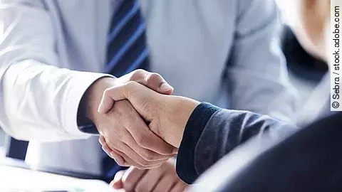 Händeschütteln zweier sich gegenübersitzenden Personen