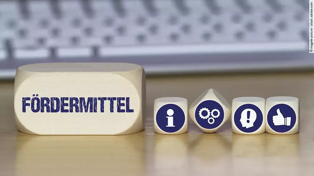 Ein Holzklotz mit der Aufschrift Fördermittel. Daneben liegen Würfel mit den Symbolen i (für Information), Zahnrädchen, ein Kopf mit einem Ausrufezeichen und ein Daumen-hoch.