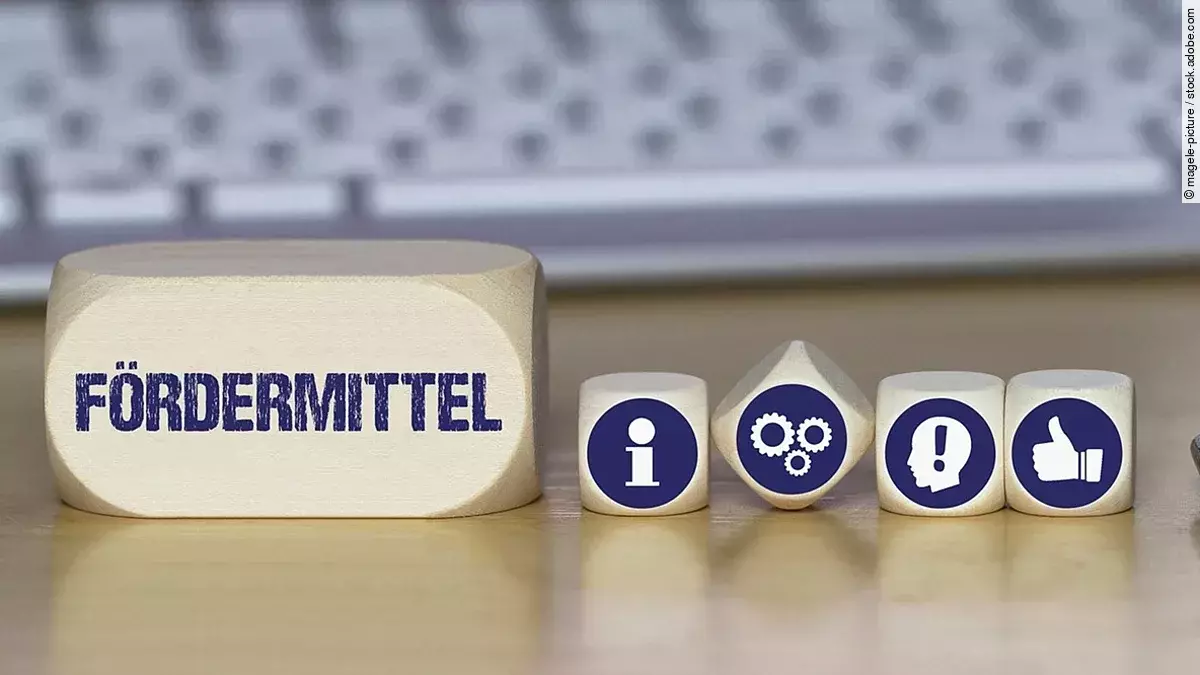 Ein Holzklotz mit der Aufschrift Fördermittel. Daneben liegen Würfel mit den Symbolen i (für Information), Zahnrädchen, ein Kopf mit einem Ausrufezeichen und ein Daumen-hoch.
