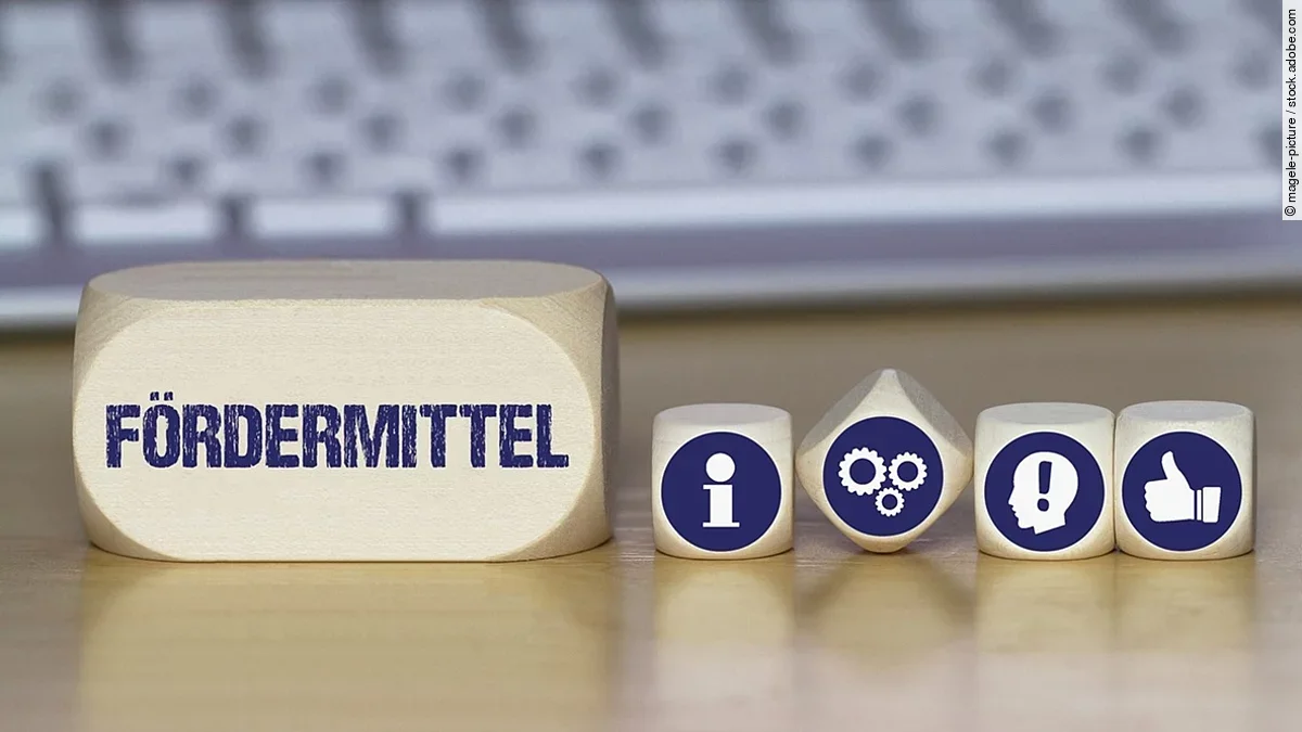 Ein Holzklotz mit der Aufschrift Fördermittel. Daneben liegen Würfel mit den Symbolen i (für Information), Zahnrädchen, ein Kopf mit einem Ausrufezeichen und ein Daumen-hoch.