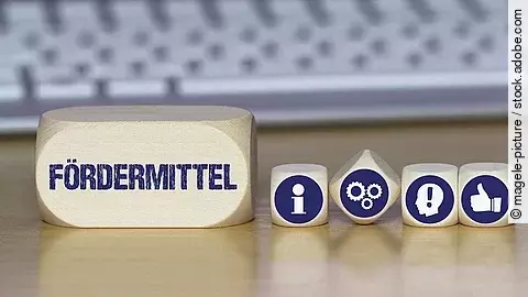 Ein Holzklotz mit der Aufschrift Fördermittel. Daneben liegen Würfel mit den Symbolen i (für Information), Zahnrädchen, ein Kopf mit einem Ausrufezeichen und ein Daumen-hoch.