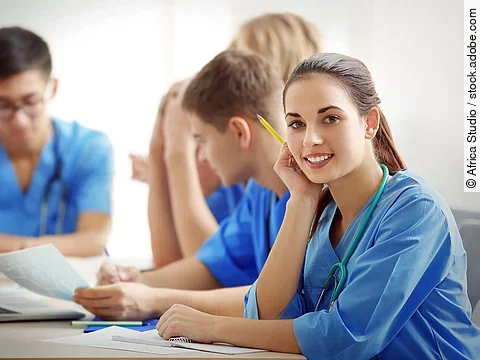 Eine Gruppe an (Pflege-)Auszubildenden sitzt nebeneinander am Tisch.