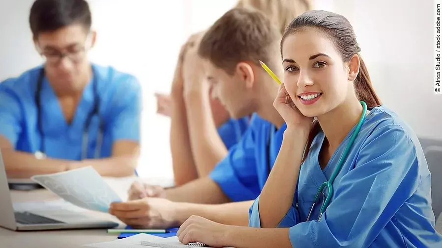 Eine Gruppe an (Pflege-)Auszubildenden sitzt nebeneinander am Tisch.