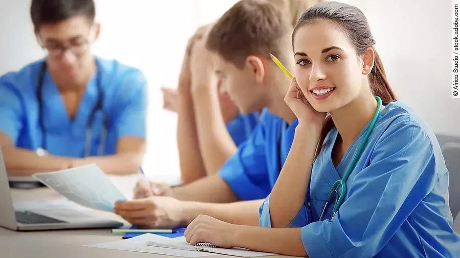 Ausbildung Eine Gruppe an (Pflege-)Auszubildenden sitzt nebeneinander am Tisch.