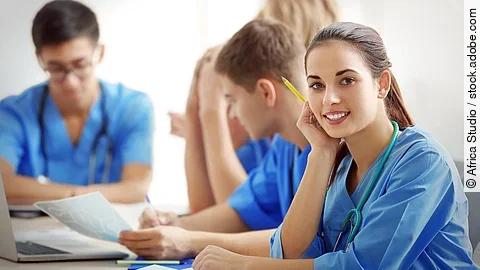 Eine Gruppe an (Pflege-)Auszubildenden sitzt nebeneinander am Tisch.