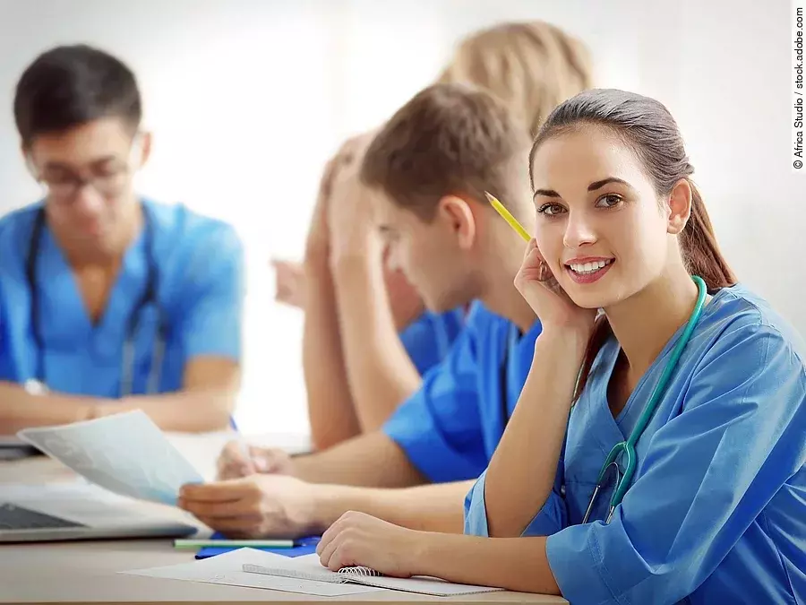 Eine Gruppe an (Pflege-)Auszubildenden sitzt nebeneinander am Tisch.