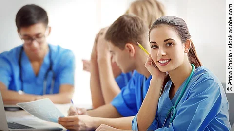 Eine Gruppe an (Pflege-)Auszubildenden sitzt nebeneinander am Tisch.