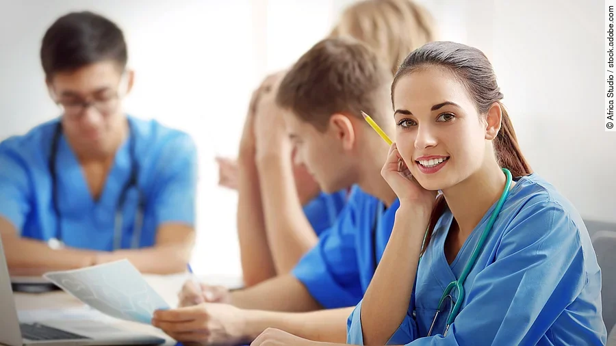 Eine Gruppe an (Pflege-)Auszubildenden sitzt nebeneinander am Tisch.