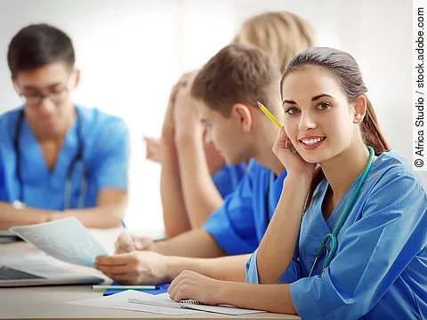Eine Gruppe an (Pflege-)Auszubildenden sitzt nebeneinander am Tisch.