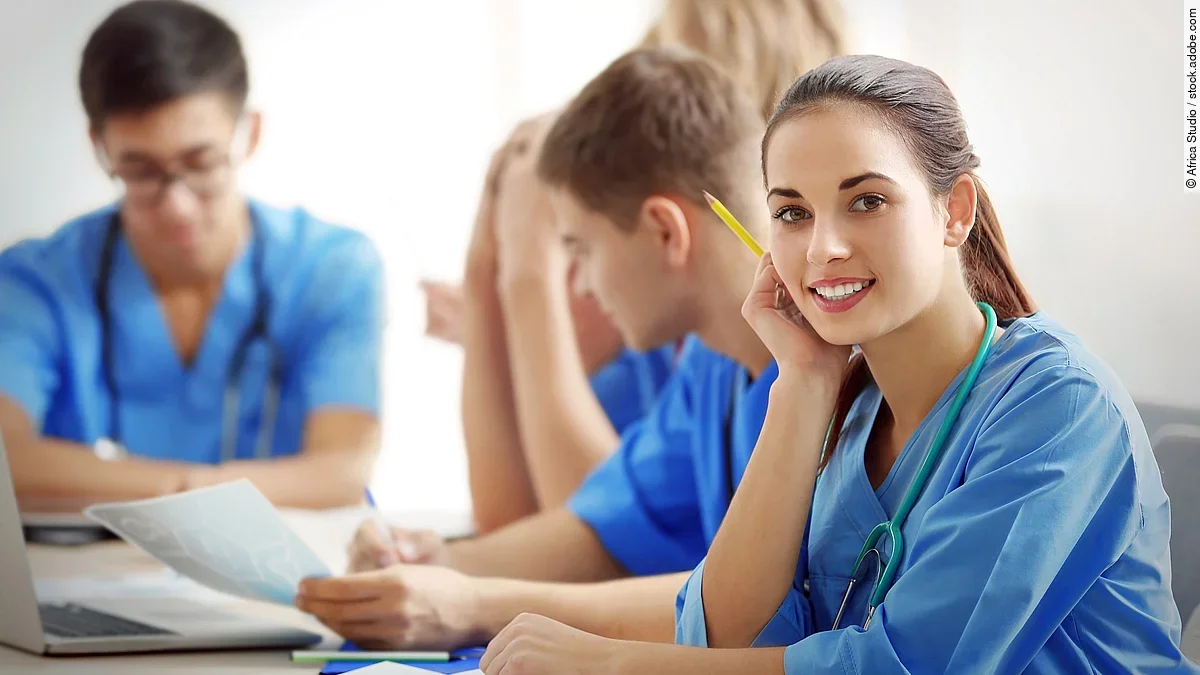 Ausbildung Eine Gruppe an (Pflege-)Auszubildenden sitzt nebeneinander am Tisch.