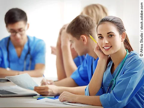 Eine Gruppe an (Pflege-)Auszubildenden sitzt nebeneinander am Tisch.