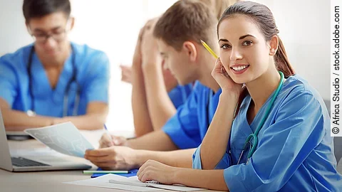 Ausbildung Eine Gruppe an (Pflege-)Auszubildenden sitzt nebeneinander am Tisch.