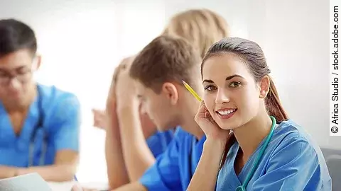 Eine Gruppe an (Pflege-)Auszubildenden sitzt nebeneinander am Tisch.