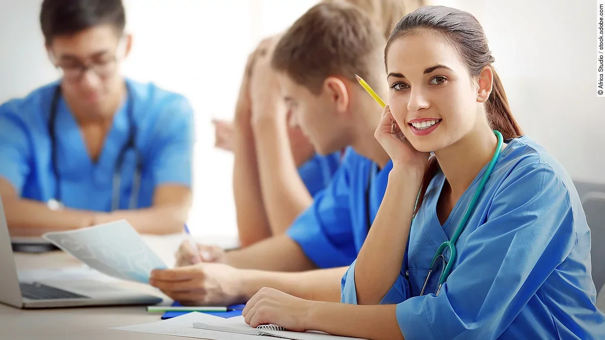 Eine Gruppe an (Pflege-)Auszubildenden sitzt nebeneinander am Tisch.