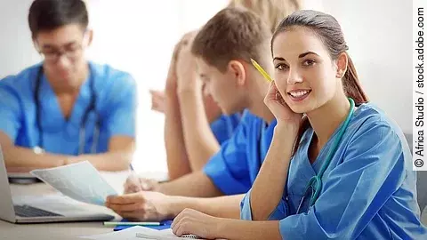 Eine Gruppe an (Pflege-)Auszubildenden sitzt nebeneinander am Tisch.