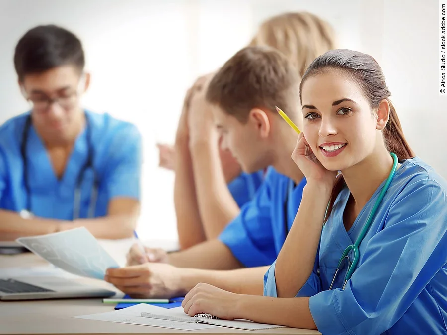 Eine Gruppe an (Pflege-)Auszubildenden sitzt nebeneinander am Tisch.