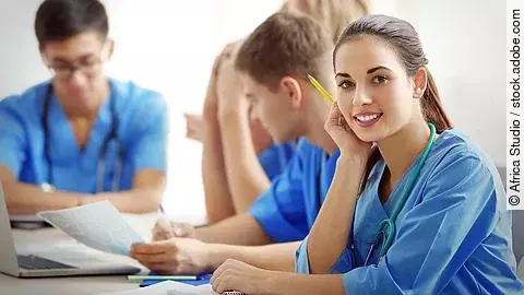 Ausbildung Eine Gruppe an (Pflege-)Auszubildenden sitzt nebeneinander am Tisch.