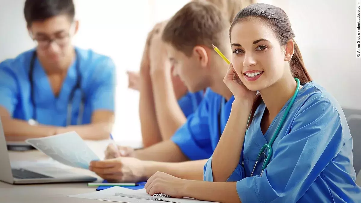 Ausbildung Eine Gruppe an (Pflege-)Auszubildenden sitzt nebeneinander am Tisch.