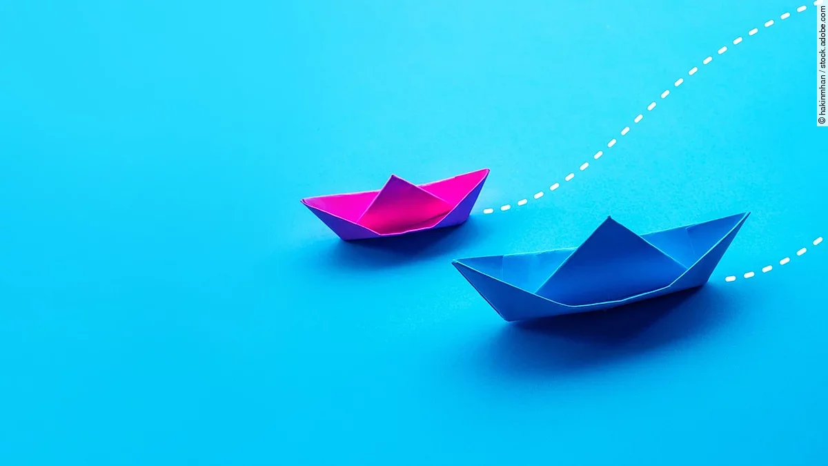 Zwei Papierboote in pink und blau fahren gemeinsam in eine Richtung.