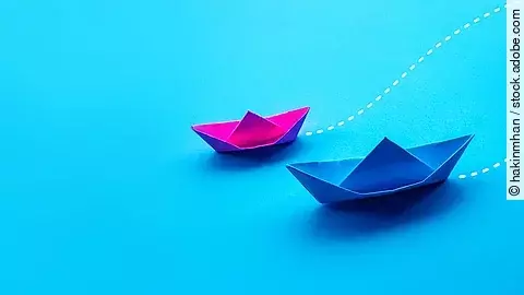 Zwei Papierboote in pink und blau fahren gemeinsam in eine Richtung.