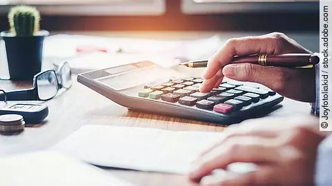 Rechnung Ein Mann tippt etwas in einen Taschenrechner. Vor ihm liegt ein Blatt Papier.