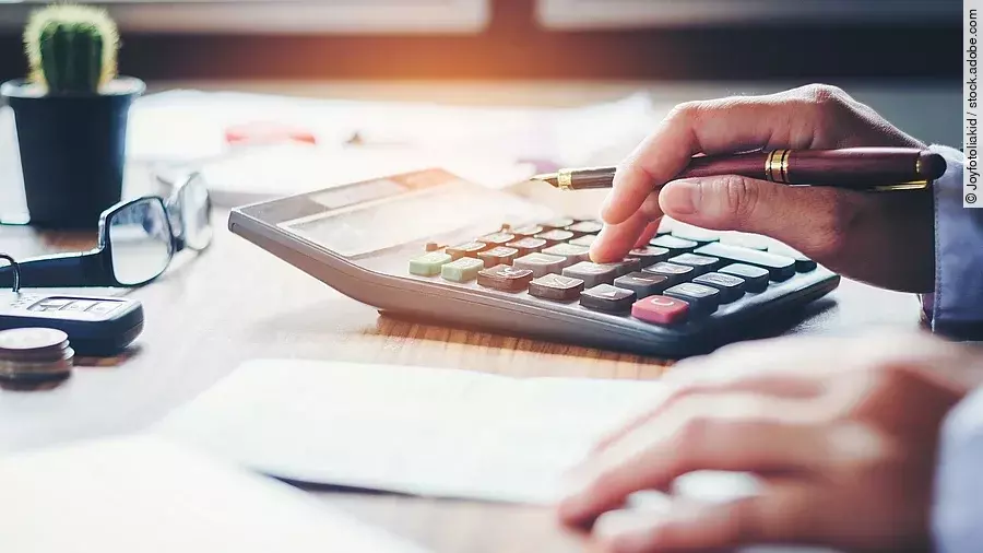 Ein Mann tippt etwas in einen Taschenrechner. Vor ihm liegt ein Blatt Papier.