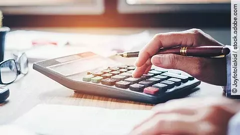 Ein Mann tippt etwas in einen Taschenrechner. Vor ihm liegt ein Blatt Papier.