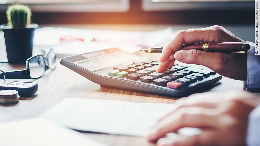 Ein Mann tippt etwas in einen Taschenrechner. Vor ihm liegt ein Blatt Papier.