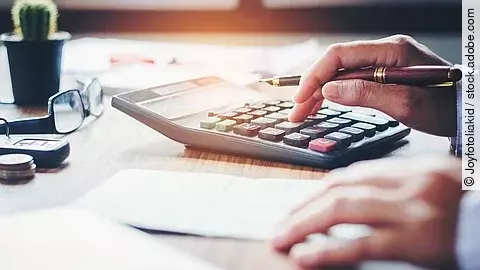 Ein Mann tippt etwas in einen Taschenrechner. Vor ihm liegt ein Blatt Papier.