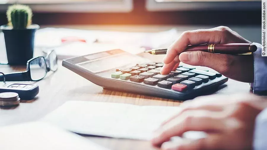 Ein Mann tippt etwas in einen Taschenrechner. Vor ihm liegt ein Blatt Papier.